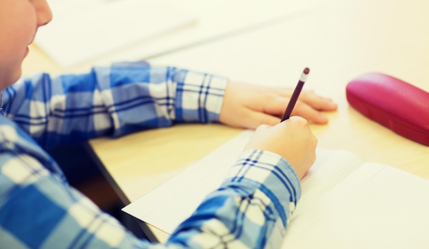 educación, escuela primaria, aprendizaje y concepto de personas - cierre de un pequeño escolar con prueba de escritura de cuaderno y lápiz en la escuela