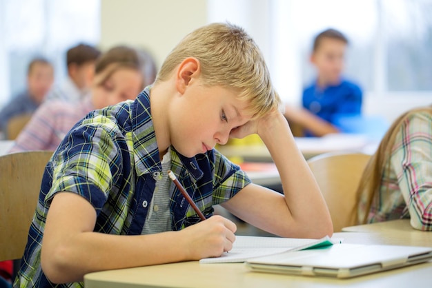 educación, escuela primaria, aprendizaje y concepto de personas - grupo de escolares con bolígrafos y cuadernos escribiendo pruebas en el aula