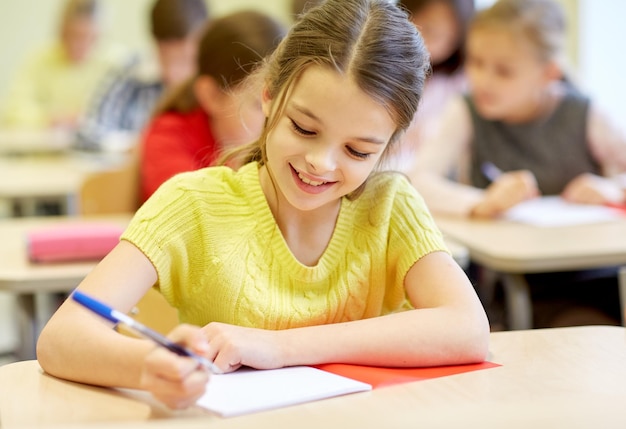 educación, escuela primaria, aprendizaje y concepto de personas - grupo de escolares con bolígrafos y cuadernos escribiendo pruebas en el aula