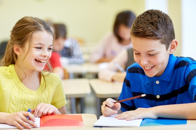 educación, escuela primaria, aprendizaje y concepto de personas - grupo de escolares con bolígrafos y cuadernos escribiendo pruebas en el aula