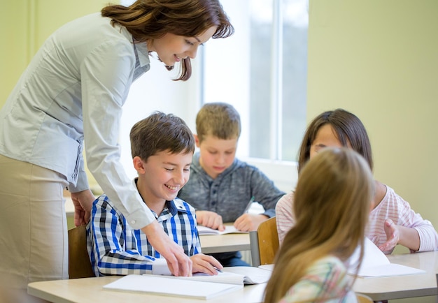 educación, escuela primaria, aprendizaje y concepto de personas - maestro que ayuda a los escolares a escribir pruebas en el aula