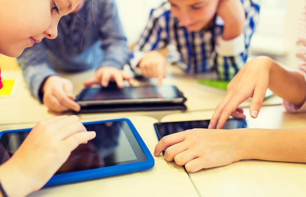 educación, escuela primaria, aprendizaje, tecnología y concepto de la gente - cerca de los niños de la escuela con computadoras tablet pc divirtiéndose y jugando en el descanso en el aula