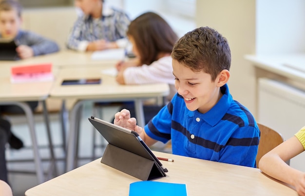 educación, escuela primaria, aprendizaje, tecnología y concepto de personas - colegial pequeño con computadora de tablet pc en descanso en el aula