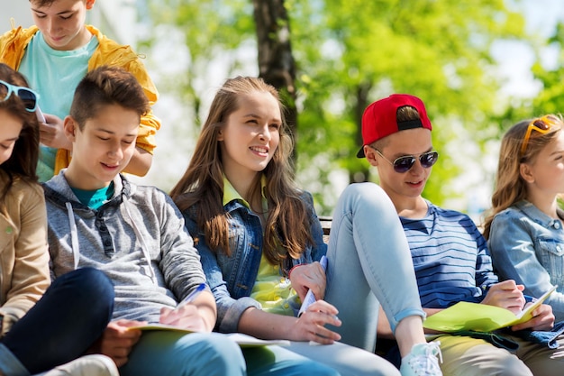 educación, escuela secundaria y concepto de personas - grupo de estudiantes adolescentes felices con cuadernos aprendiendo en el patio del campus