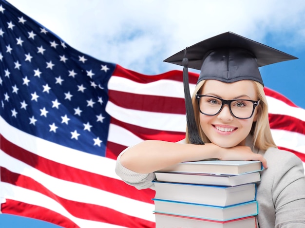 educación, escuela secundaria, conocimiento y concepto de la gente - foto de una estudiante feliz o una mujer con gorra de zanjadora con una pila de libros sobre el fondo de la bandera estadounidense