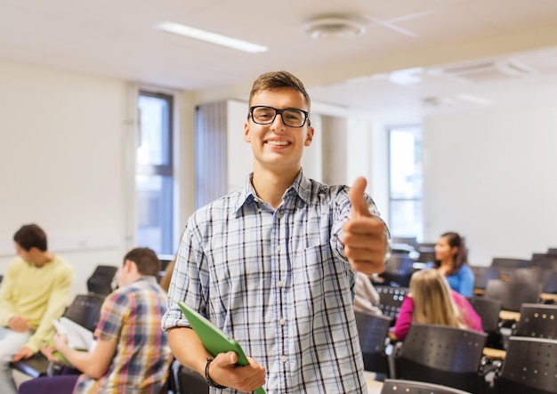 educación, escuela secundaria, gesto y concepto de personas - grupo de estudiantes sonrientes con blocs de notas que muestran los pulgares hacia arriba en la sala de conferencias