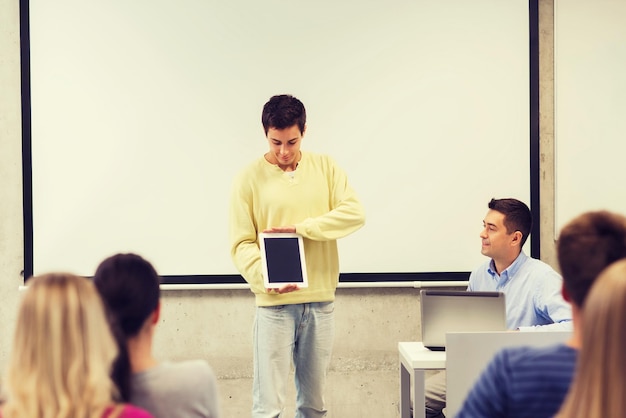 educación, escuela secundaria, tecnología y concepto de personas - estudiante sonriente con tablet pc, computadora portátil parado frente a los estudiantes y profesor en el aula