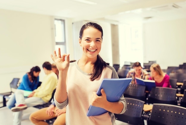 educación, escuela secundaria, trabajo en equipo y concepto de personas - grupo de estudiantes sonrientes con blocs de notas que muestran un gesto correcto en la sala de conferencias