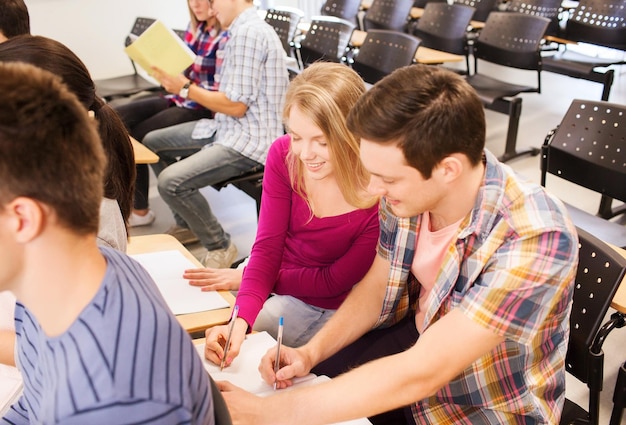 educación, escuela secundaria, trabajo en equipo y concepto de personas - grupo de estudiantes sonrientes con blocs de notas sentados en la sala de conferencias