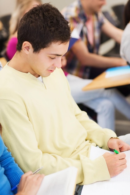 educación, escuela secundaria, trabajo en equipo y concepto de personas - grupo de estudiantes sonrientes con cuadernos y libros escribiendo en la sala de conferencias