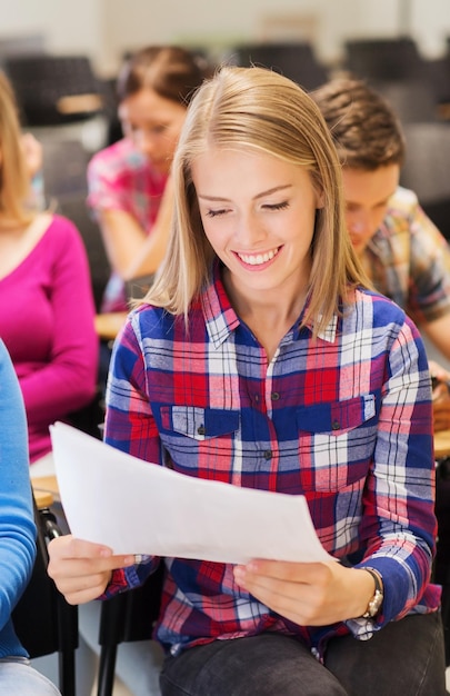 educación, escuela secundaria, trabajo en equipo y concepto de personas - grupo de estudiantes sonrientes con papel y bolígrafo sentados en la sala de conferencias y escribiendo