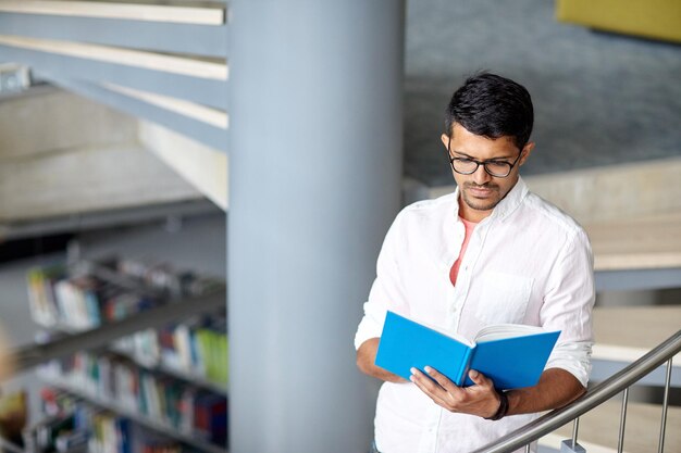 educación, escuela secundaria, universidad, aprendizaje y concepto de la gente - estudiante hindú o joven leyendo un libro en las escaleras de la biblioteca