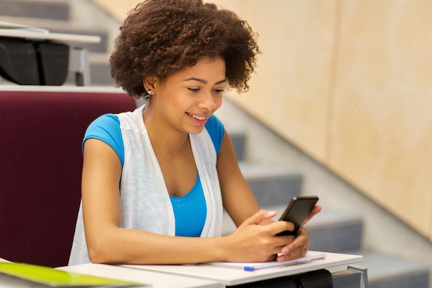 educación, escuela secundaria, universidad, aprendizaje y concepto de personas - estudiante africana con teléfono inteligente en conferencia