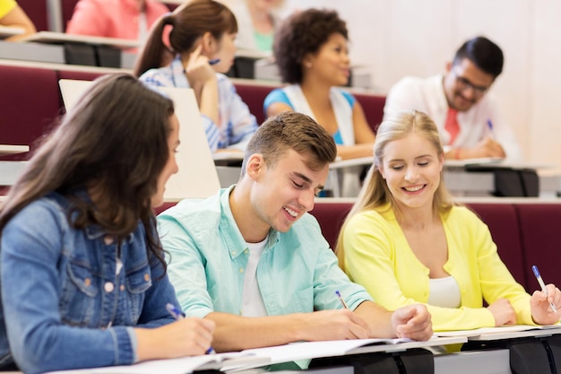 educación, escuela secundaria, universidad, aprendizaje y concepto de personas - grupo de estudiantes internacionales con cuadernos escribiendo en la sala de conferencias