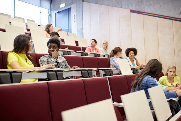 educación, escuela secundaria, universidad, aprendizaje y concepto de personas - grupo de estudiantes internacionales con cuadernos hablando en la sala de conferencias