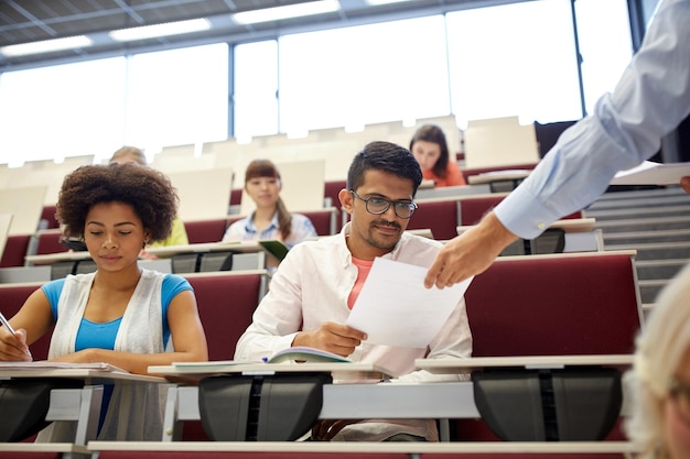 educación, escuela secundaria, universidad, aprendizaje y concepto de personas - profesor dando pruebas a los estudiantes en la conferencia