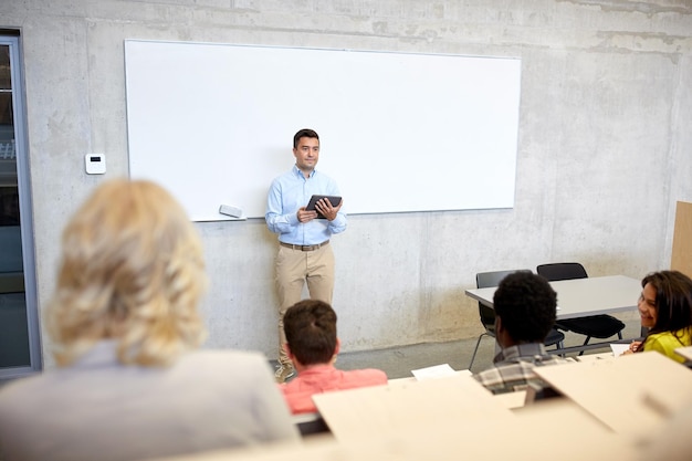 educación, escuela secundaria, universidad, enseñanza y concepto de personas - grupo de estudiantes internacionales y profesor con computadora de tablet pc de pie en la pizarra blanca en la conferencia