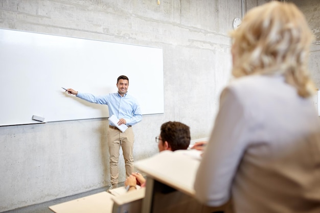 educación, escuela secundaria, universidad, enseñanza y concepto de personas - grupo de estudiantes y profesores con marcador de pie en la pizarra blanca en la conferencia