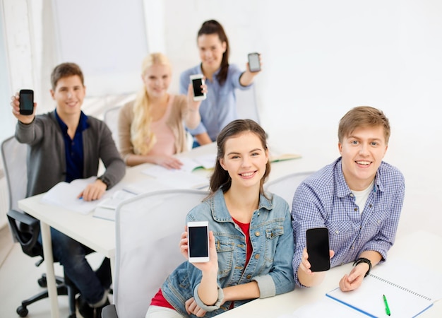 educación, escuela, tecnología y concepto de Internet - estudiantes sonrientes que muestran pantallas negras de teléfonos inteligentes en blanco en la escuela