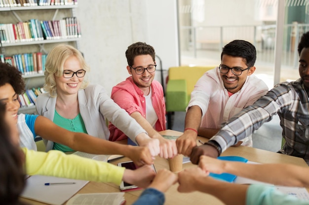 Foto educación, escuela, trabajo en equipo y concepto de personas - grupo de estudiantes internacionales sentados en la mesa y haciendo puñetazos