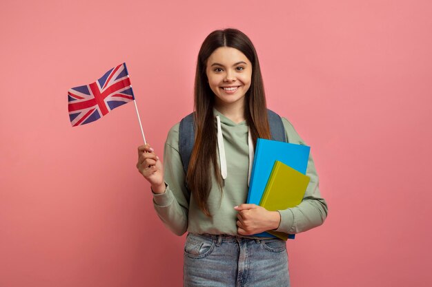 Educación en el extranjero chica adolescente sonriente posando con cuadernos de trabajo y bandera británica