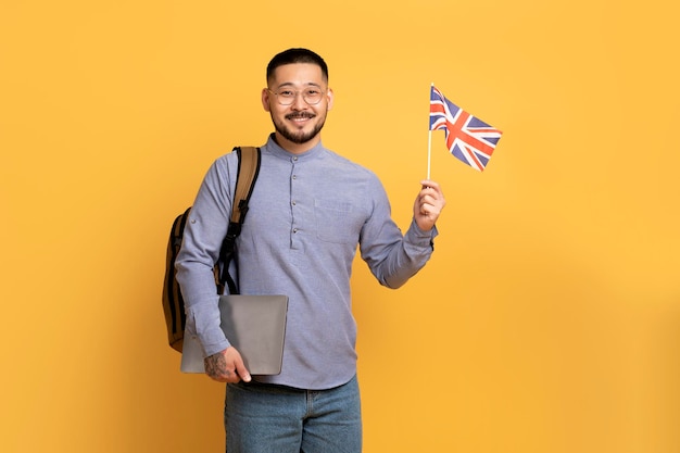 Educación en el extranjero Sonriente joven asiático posando con portátil y bandera británica