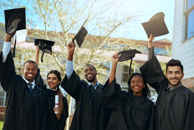 Educación para ganar Retrato de un grupo de jóvenes estudiantes felices quitándose el sombrero el día de la graduación