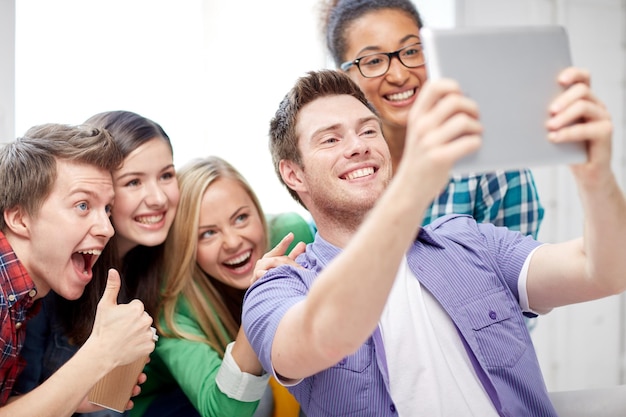 educación, gente, amistad, tecnología y concepto de aprendizaje - grupo de felices estudiantes internacionales de secundaria con tablet pc tomando selfie en el aula y mostrando los pulgares hacia arriba