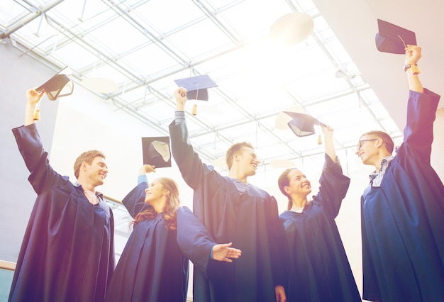 educación, graduación y concepto de personas - grupo de estudiantes felices o solteros en batas que agitan mortarboards en la escuela