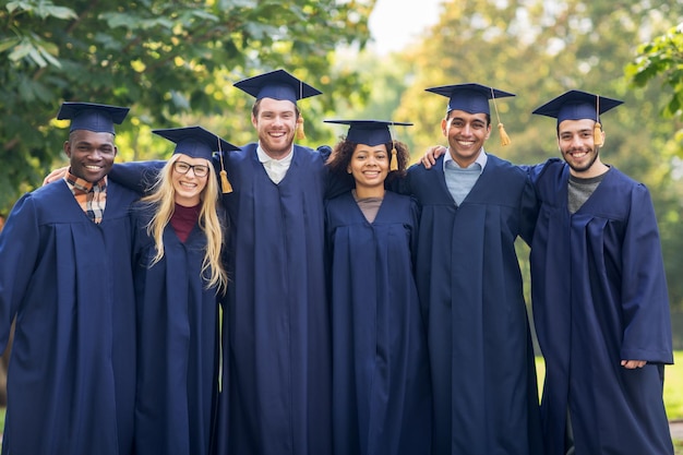 educación, graduación y concepto de personas - grupo de estudiantes internacionales felices en juntas de mortero y vestidos de soltero al aire libre