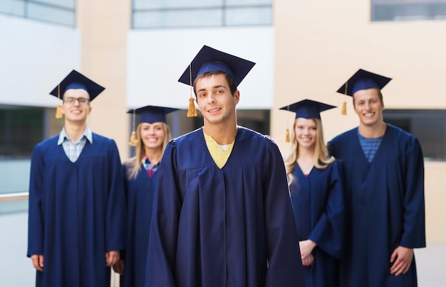 educación, graduación y concepto de personas - grupo de estudiantes sonrientes en mortarboards y batas al aire libre