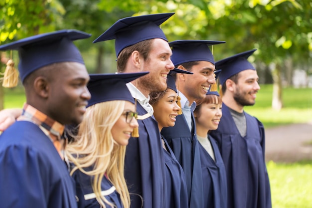 Foto educación graduación y la gente concepto grupo de estudiantes internacionales felices en tablas de mortero y vestidos de soltero al aire libre