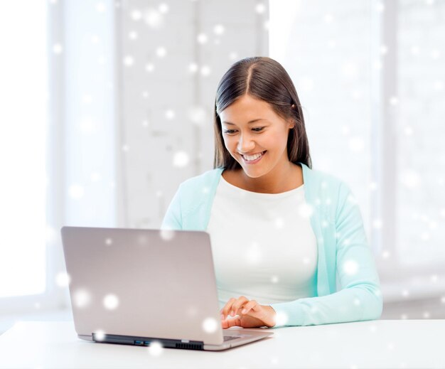 educación, invierno, tecnología y concepto de personas - mujer joven sonriente con computadora portátil en el interior