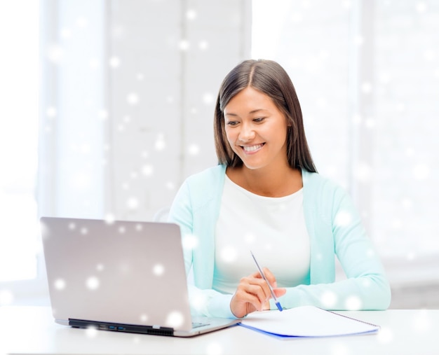 educación, invierno, tecnología y concepto de personas - mujer joven sonriente con computadora portátil y portátil en el interior