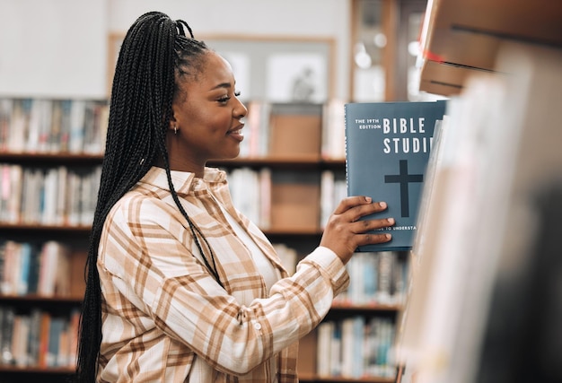 Educación de libros de religión y mujer negra en una biblioteca para investigar el estudio de Dios y el conocimiento de la Biblia en la universidad Sonrisa de aprendizaje y estudiante africano con decisión de libros sobre una beca