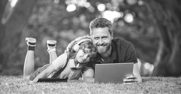 Foto educación en línea en una computadora portátil, padre e hijo usan tecnología de comunicación moderna en el parque, feliz día familiar, infancia y paternidad, niño feliz, escucha música con auriculares, seminario web, videolección