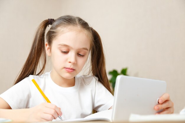 Foto educación en línea a distancia. colegiala estudiando en casa con portátil tableta digital y haciendo los deberes escolares.