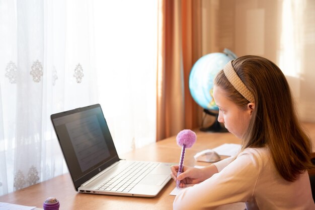 Foto educación en línea de niños una colegiala enseña una lección en línea usando una conferencia de video chat con una computadora portátil con un maestro en casa estudiando participando en una conferencia en línea sentada en el escritorio