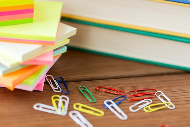 Foto educación, material escolar, papelería y concepto de objeto - cierre de soporte o vidrio con herramientas de escritura y libro con tijeras sobre mesa de madera