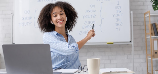 Educación moderna a distancia Mujer afroamericana alegre señala a la pizarra y explica las reglas del inglés