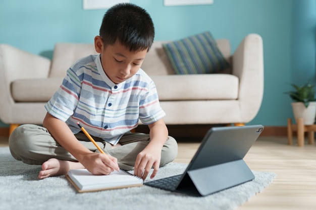 Foto educación. niño asiático aprendiendo y haciendo deberes con el profesor en línea en tableta digital en casa