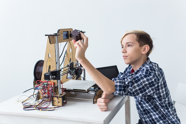 Foto educación, niños, concepto de tecnología - muchacho adolescente está imprimiendo en una impresora 3d.