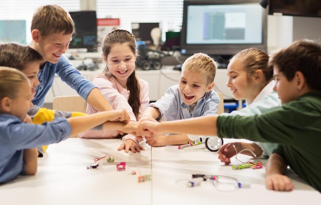 Foto educación, niños, tecnología, ciencia y concepto de personas - grupo de niños felices construyendo robots en la lección de robótica y haciendo puñetazos