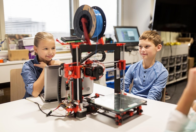 Educación, niños, tecnología, ciencia y concepto de personas: grupo de niños felices con impresora 3D y computadora portátil en la lección de la escuela de robótica