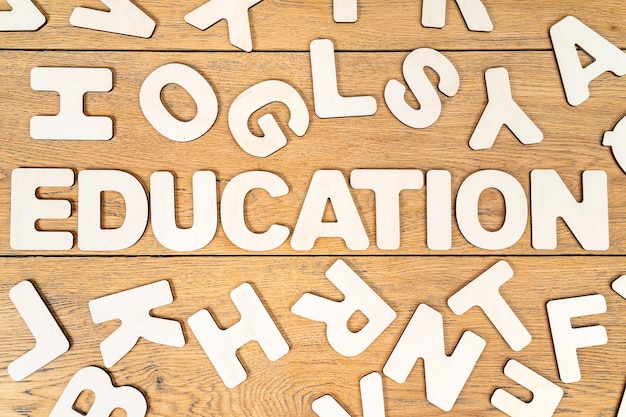 la educación de la palabra se presenta con letras de madera en medio de varias letras esparcidas al azar sobre una mesa de madera
