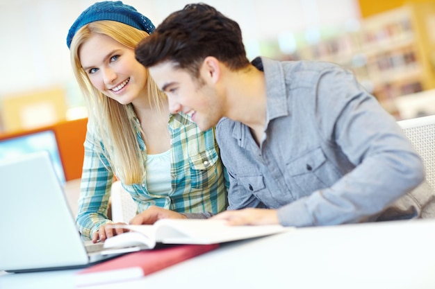 Educación portátil y sonrisa con un par de amigos en la biblioteca en el campus universitario o universitario para el aprendizaje Investigación informática y estudio con estudiantes felices en el escritorio de la escuela para la beca juntos