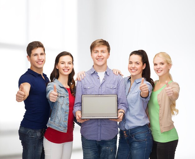 educación, publicidad y concepto de nueva tecnología - estudiantes sonrientes con pantalla en blanco de computadora portátil mostrando los pulgares hacia arriba