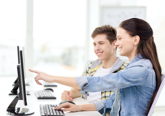 educación, tecnología y concepto escolar - dos estudiantes sonrientes en clase de computación, niña señalando con el dedo a la pantalla