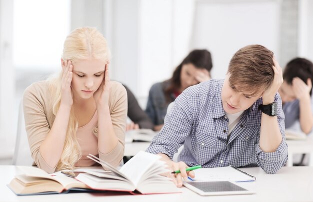 educación, tecnología y concepto de internet - estudiantes cansados con tablet pc, libros y cuadernos preparándose para el examen