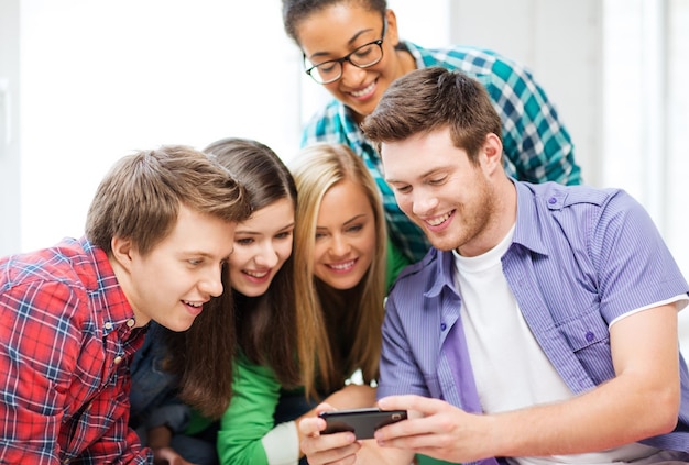 Foto educación y tecnología - grupo de estudiantes mirando el teléfono inteligente en la escuela